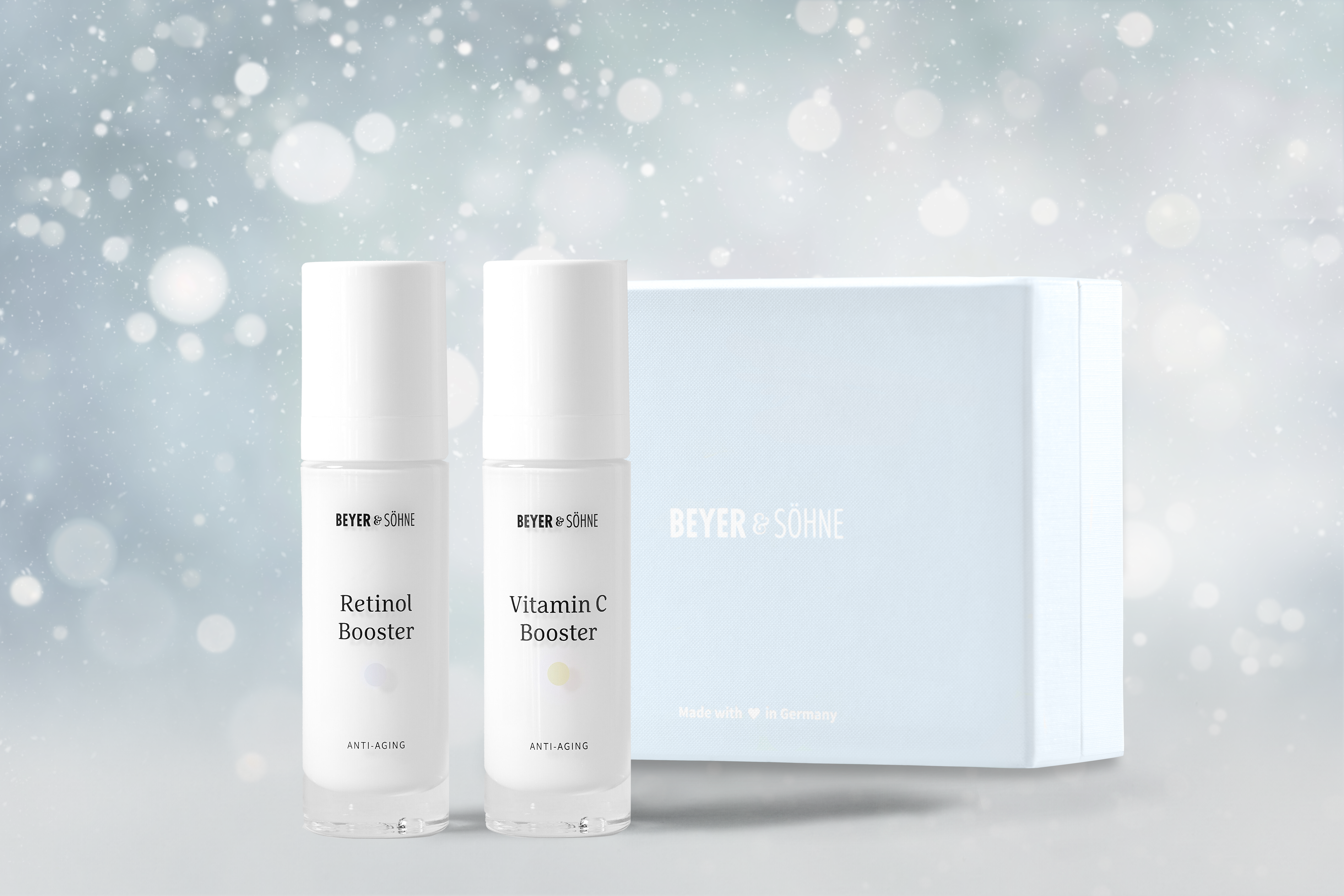 Retinol Booster und Vitamin C Booster in hochwertigen Glasspendern von Beyer & Söhne vor himmelblauer Geschenkbox und weihnachtlich gestimmten Hintergrund mit Schneeflocken.